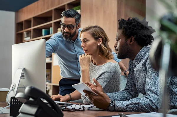 Three colleagues reviewing a project together at a desktop computer.